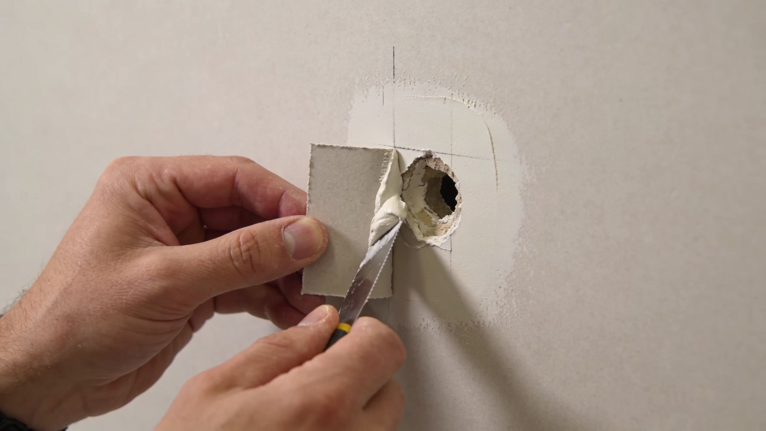 A close-up view of a person applying joint compound to a patch to repair a drywall hole.