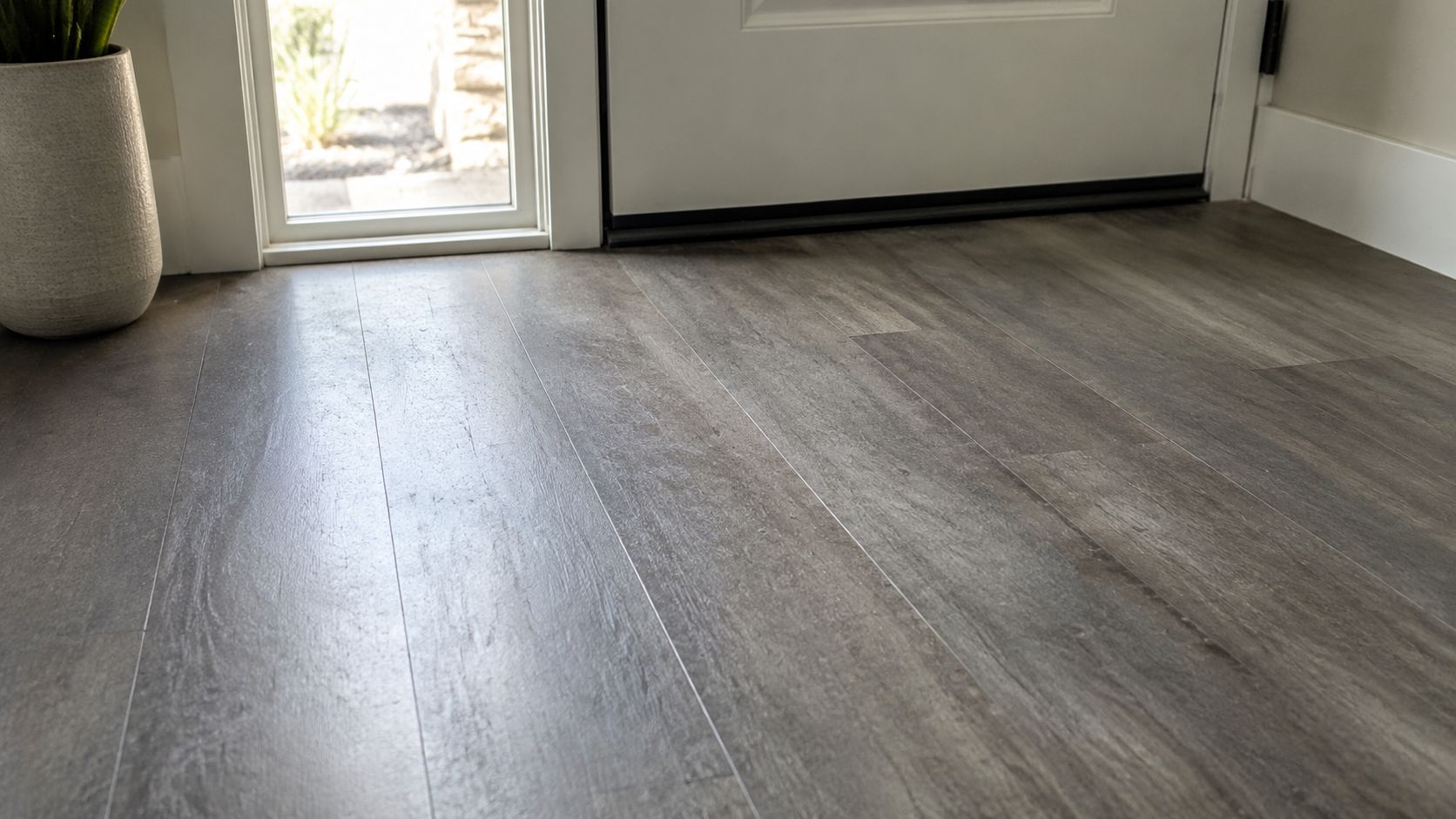 A close up view of modern grey wood-look vinyl plank flooring installed in a residential home entryway.